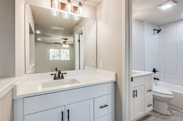 full bathroom with ceiling fan, tiled shower / bath, vanity, and toilet