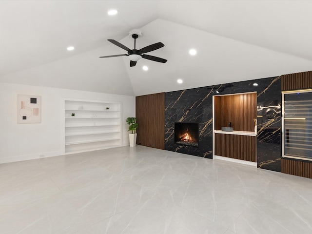 unfurnished living room with built in shelves, lofted ceiling, a high end fireplace, and ceiling fan