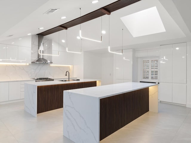 kitchen featuring pendant lighting, sink, white cabinets, a large island with sink, and wall chimney exhaust hood