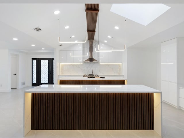 kitchen featuring wall chimney range hood, backsplash, white cabinets, and a spacious island