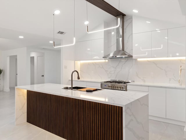 kitchen with hanging light fixtures, an island with sink, white cabinets, and wall chimney exhaust hood