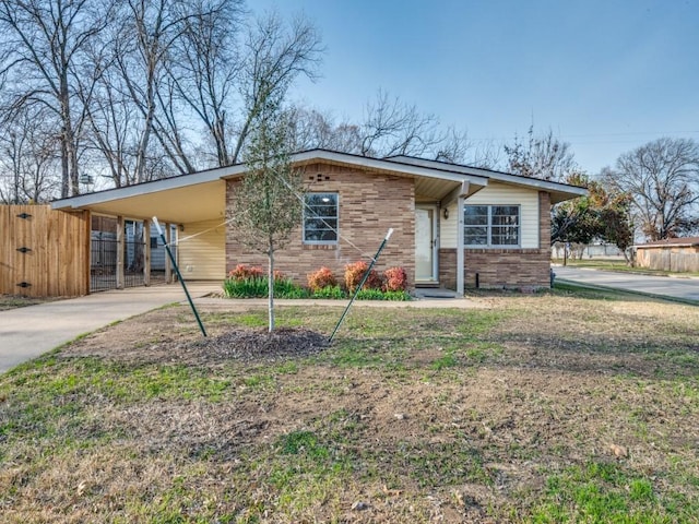 view of front of property featuring an attached carport, brick siding, fence, concrete driveway, and a front lawn