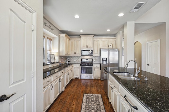 kitchen featuring dark wood-type flooring, sink, dark stone countertops, stainless steel appliances, and cream cabinets