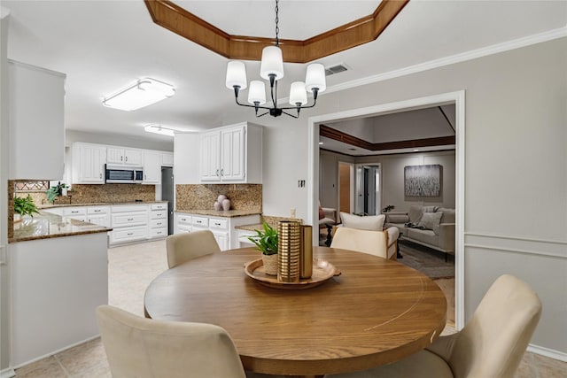 dining area with ornamental molding, a tray ceiling, and a chandelier