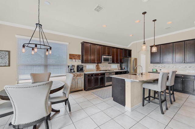 kitchen with pendant lighting, sink, appliances with stainless steel finishes, dark brown cabinets, and an island with sink