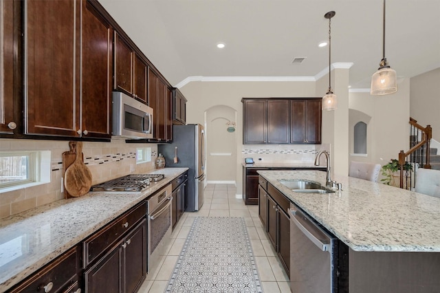 kitchen featuring pendant lighting, sink, a kitchen island with sink, stainless steel appliances, and light stone countertops