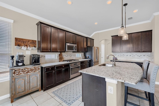 kitchen featuring appliances with stainless steel finishes, an island with sink, sink, hanging light fixtures, and dark brown cabinetry