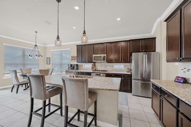 kitchen featuring stainless steel appliances, light stone counters, ornamental molding, a center island with sink, and decorative light fixtures