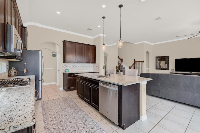 kitchen featuring sink, appliances with stainless steel finishes, hanging light fixtures, light stone counters, and an island with sink