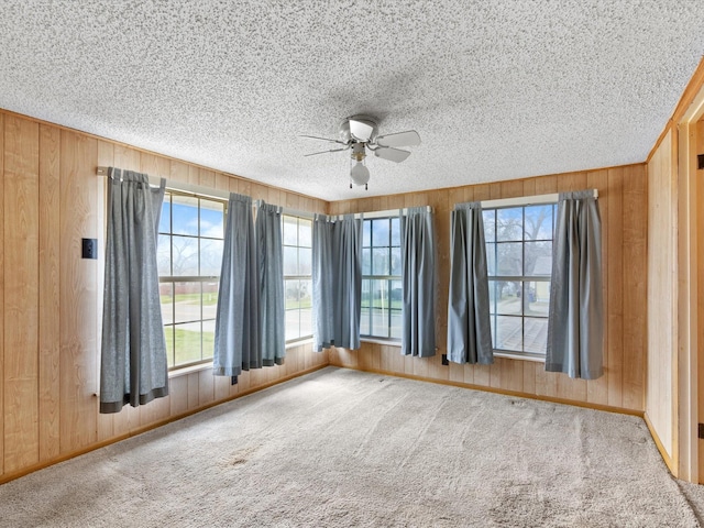 empty room with ceiling fan, carpet flooring, a textured ceiling, and wood walls