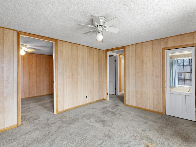 unfurnished bedroom with light carpet, ceiling fan, a textured ceiling, and wood walls