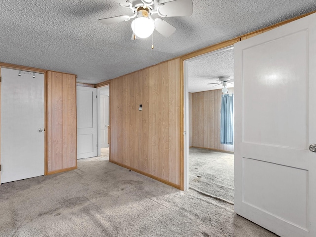 unfurnished bedroom featuring ceiling fan, light colored carpet, a textured ceiling, and wood walls