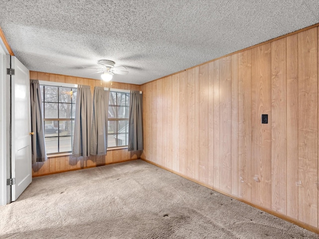 carpeted empty room featuring a textured ceiling, ceiling fan, and wood walls