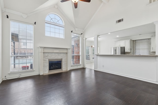 unfurnished living room with ceiling fan, high vaulted ceiling, decorative columns, dark hardwood / wood-style flooring, and a stone fireplace