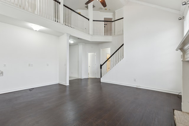 unfurnished living room with dark wood-type flooring, ceiling fan, ornamental molding, and a towering ceiling