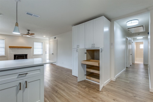 kitchen featuring ceiling fan, hanging light fixtures, a fireplace, white cabinets, and light wood-type flooring