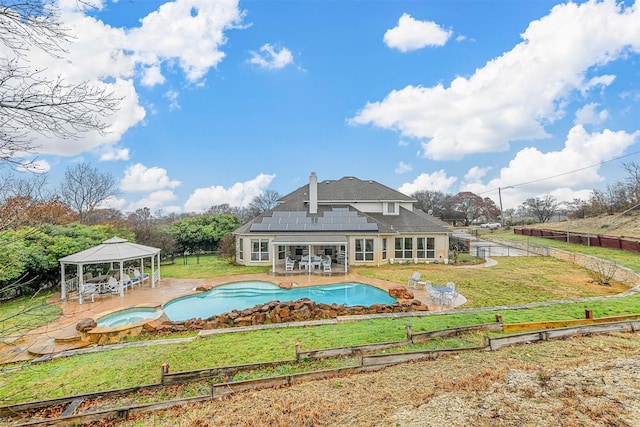 rear view of house featuring a yard, a patio, a gazebo, roof mounted solar panels, and an in ground hot tub