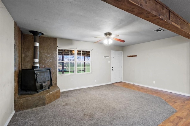 unfurnished living room featuring a textured ceiling, hardwood / wood-style flooring, ceiling fan, and a wood stove