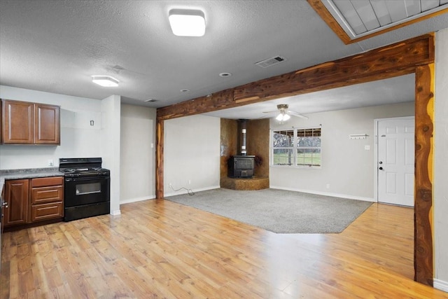 kitchen with light wood-type flooring, beam ceiling, gas stove, and a wood stove