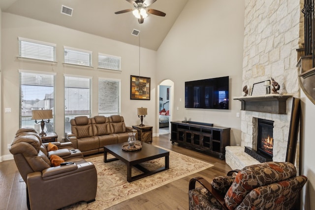 living room featuring visible vents, wood finished floors, arched walkways, a fireplace, and ceiling fan