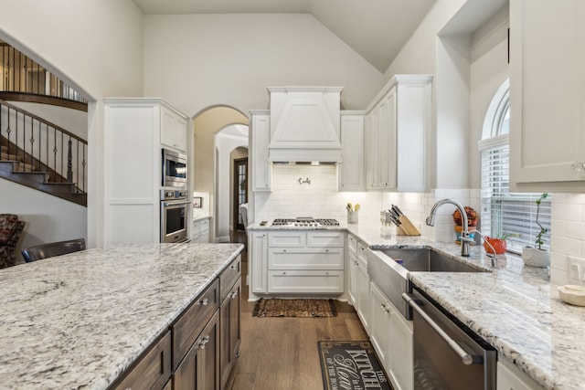 kitchen with premium range hood, light stone counters, appliances with stainless steel finishes, dark wood-style floors, and white cabinets