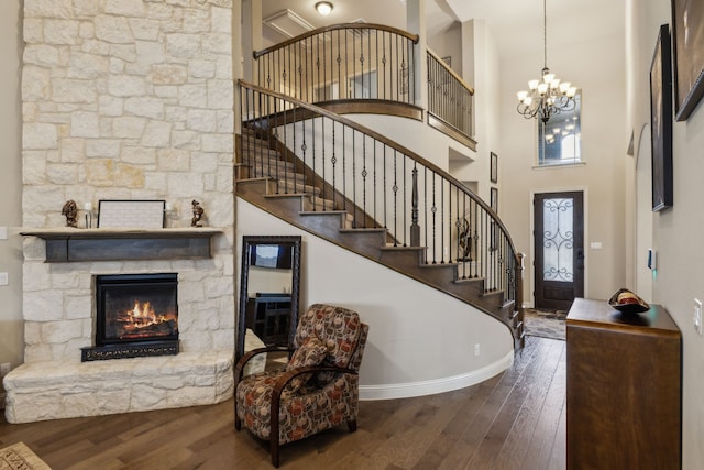 foyer with a towering ceiling, dark hardwood / wood-style floors, a stone fireplace, and a notable chandelier