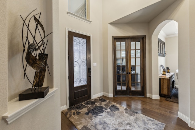 foyer entrance featuring arched walkways, french doors, baseboards, and dark wood-style flooring