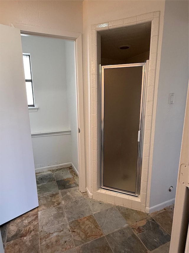 bathroom with a stall shower, stone finish floor, and baseboards