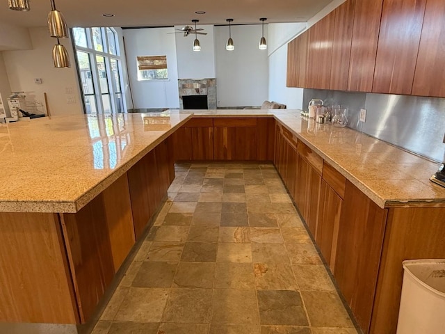 kitchen featuring stone finish flooring, a fireplace, brown cabinetry, and a ceiling fan