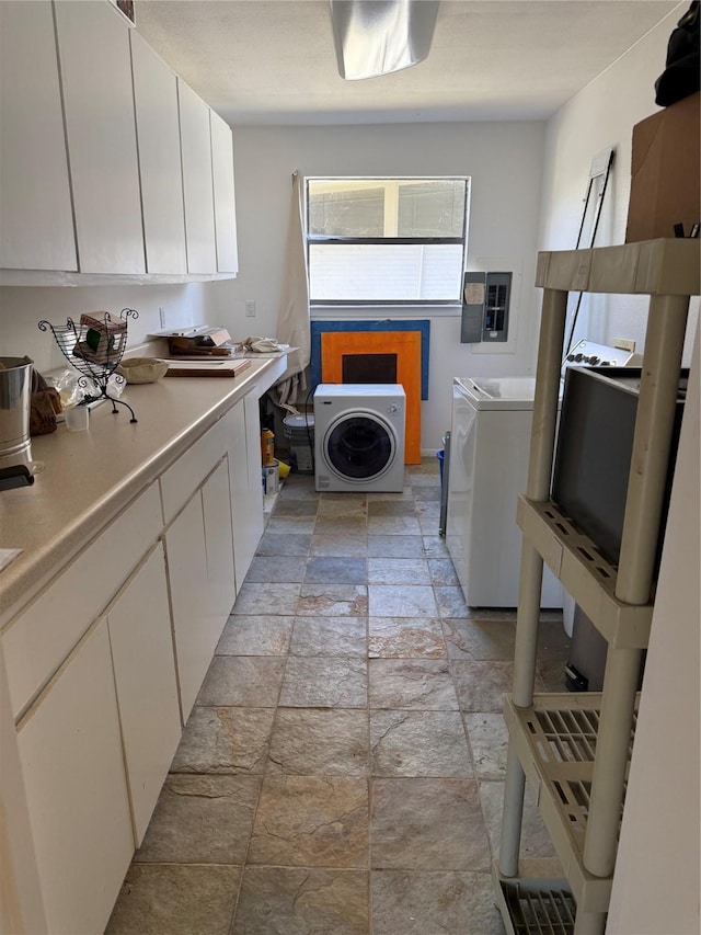 clothes washing area featuring electric panel, stone tile flooring, and washer and dryer