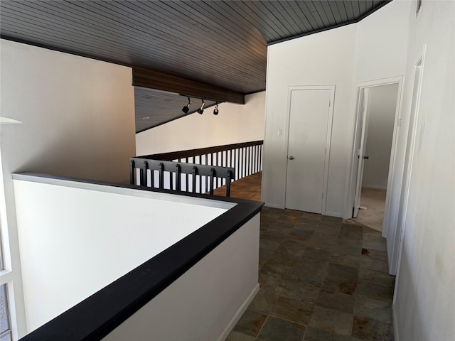 corridor featuring stone finish floor, wooden ceiling, and track lighting