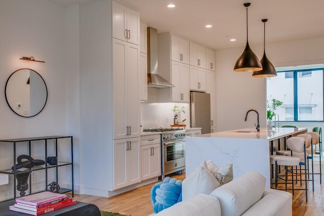 kitchen with white cabinetry, wall chimney range hood, stainless steel appliances, and sink