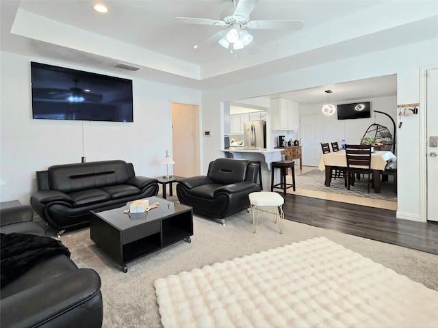 living room with hardwood / wood-style flooring, a raised ceiling, and ceiling fan