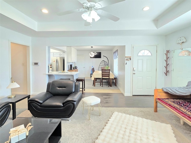 living room with a raised ceiling, ceiling fan, and light wood-type flooring