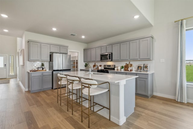 kitchen featuring gray cabinetry, an island with sink, and appliances with stainless steel finishes