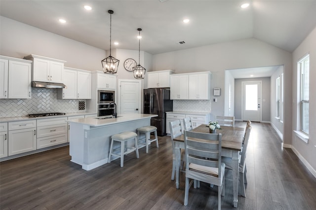 kitchen with a breakfast bar area, appliances with stainless steel finishes, hanging light fixtures, an island with sink, and white cabinets