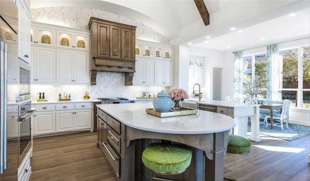 kitchen with dark wood-type flooring, white cabinetry, backsplash, vaulted ceiling with beams, and a center island