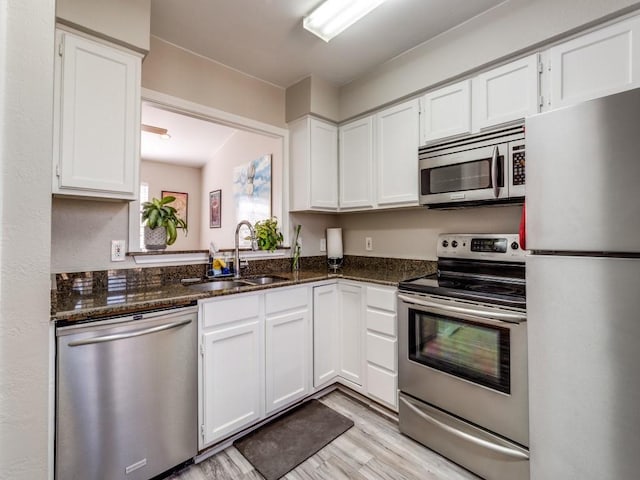 kitchen with appliances with stainless steel finishes, dark stone countertops, a sink, and white cabinets