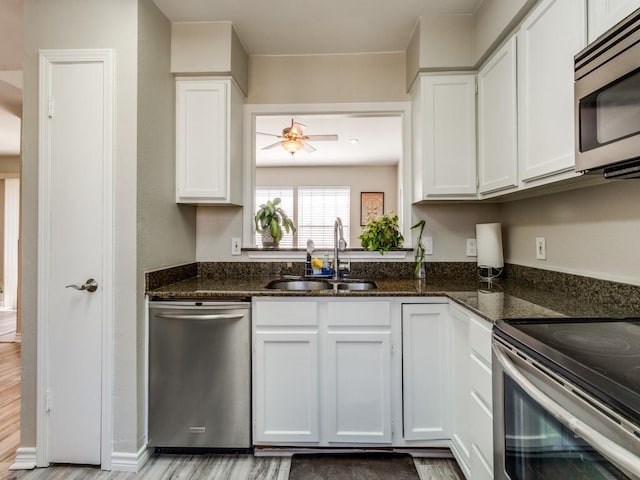 kitchen featuring stainless steel appliances, a sink, white cabinetry, a ceiling fan, and dark stone counters