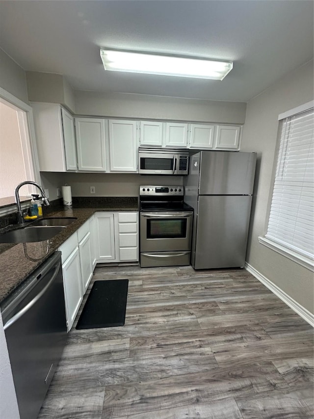 kitchen with light wood finished floors, white cabinets, appliances with stainless steel finishes, dark stone countertops, and a sink