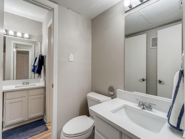 bathroom with toilet, two vanities, a sink, and wood finished floors