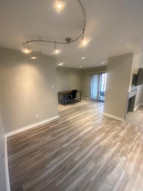 unfurnished living room with rail lighting, a fireplace, baseboards, and wood finished floors