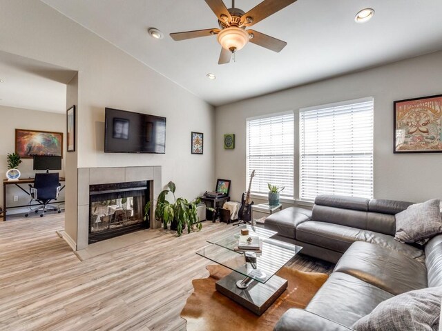 living area featuring recessed lighting, a ceiling fan, vaulted ceiling, light wood-type flooring, and a tiled fireplace