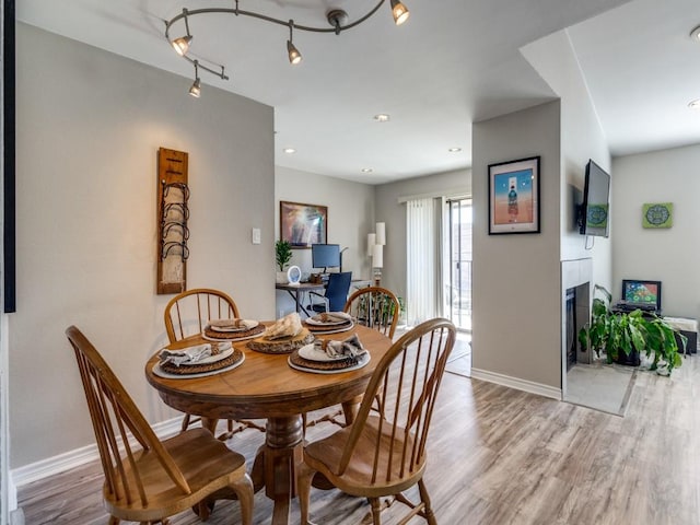 dining area with light wood finished floors, a tiled fireplace, and baseboards