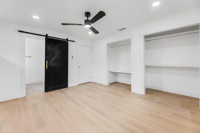 unfurnished bedroom featuring multiple closets, ceiling fan, a barn door, and light wood-type flooring