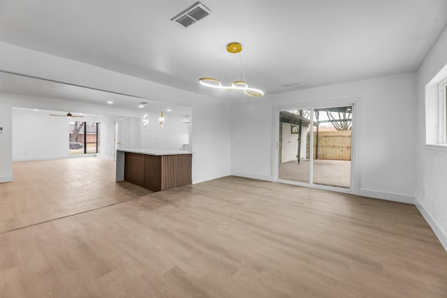 unfurnished living room featuring ceiling fan with notable chandelier and light wood-type flooring