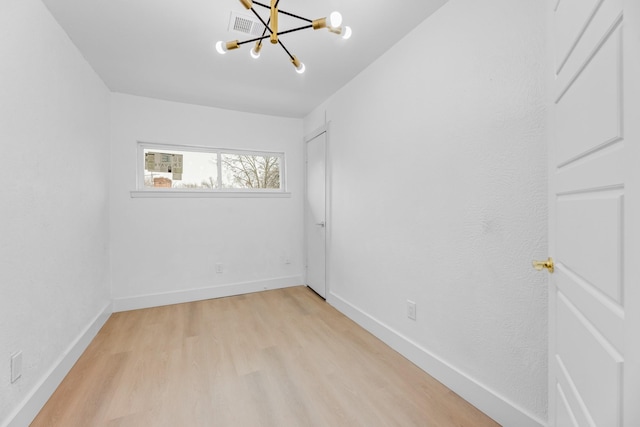 unfurnished room featuring an inviting chandelier and light hardwood / wood-style flooring