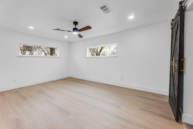 interior space with ceiling fan, a barn door, and light hardwood / wood-style flooring