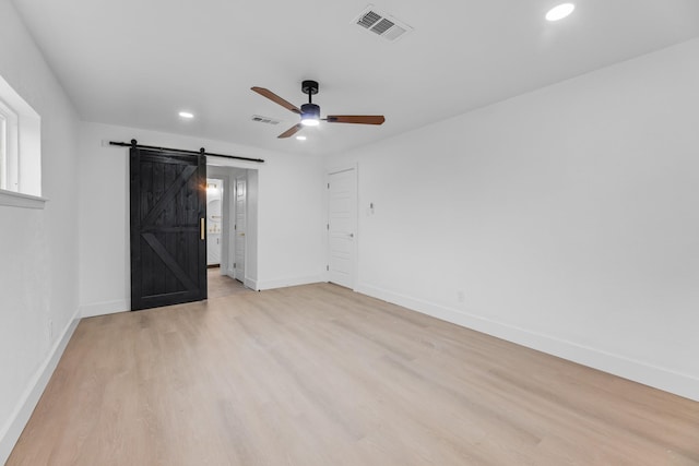 empty room featuring ceiling fan, a barn door, and light wood-type flooring