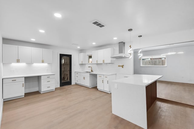 kitchen with sink, built in desk, white cabinets, and wall chimney exhaust hood